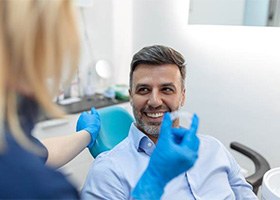 Dentist in blue gloves holding Invisalign speaking with patient in blue shirt