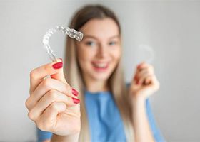 Woman in blue shirt with red nails holding two Invisalign trays