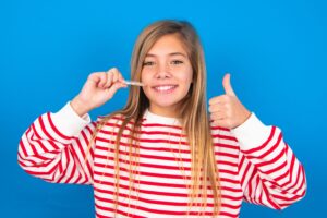 Teenager with long hair in red and white striped sweater giving thumbs up and holding Invisalign