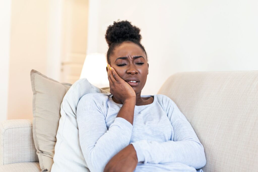 Woman on couch holding hand to her jaw in pain